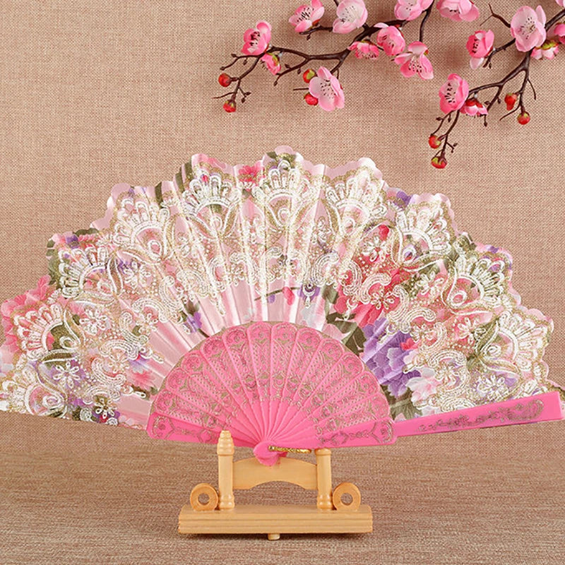 Pink and purple silk flower folding fan with intricate patterns displayed on a wooden stand.