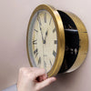A hand holds a vintage gold-toned clock with a clear face, displaying the quartz movement inside.