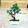 Artificial bonsai tree decoration with green leaves and white blossoms displayed in a white rectangular pot.