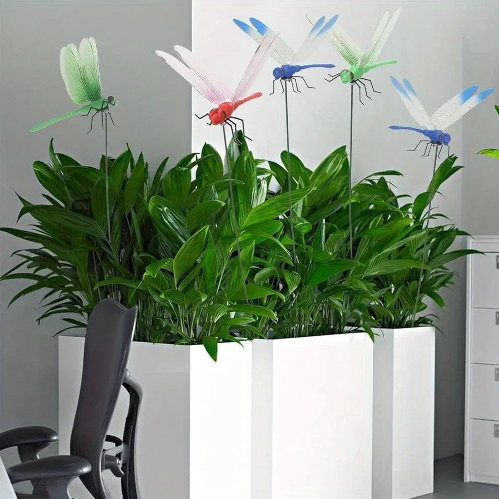 A display of realistic dragonfly hat clips in various colors, including green, pink, red, and blue, arranged in lush green fo
