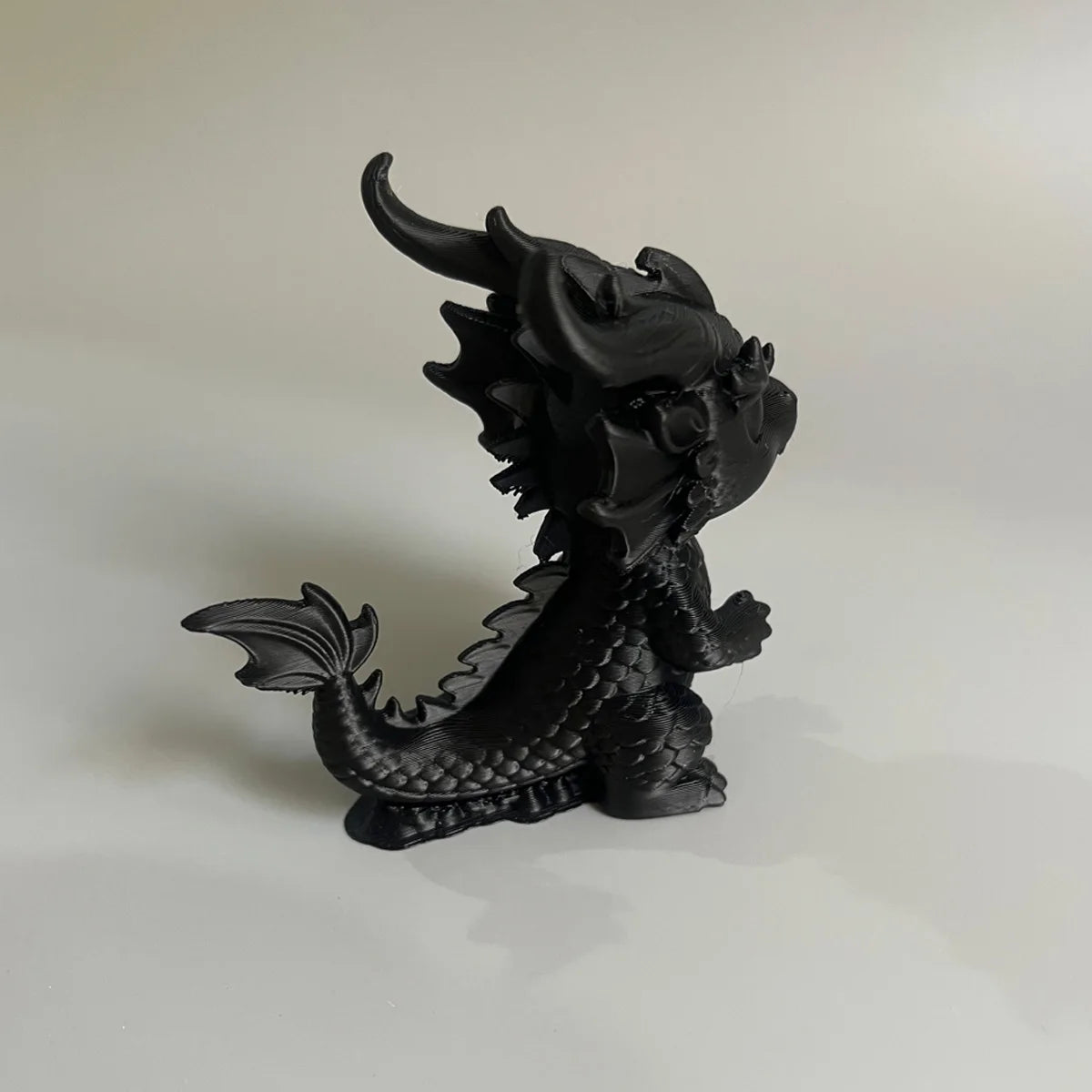 Figurine miniature de dragon noir aux cornes et écailles, exposée sur une surface blanche.