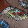 A close-up of an elegant plum blossom folding fan with intricate lace and floral patterns on a dark wooden surface.