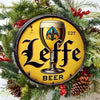 A vintage metal tin sign featuring the Leffe Beer logo in black and gold on a yellow background, used as holiday wreath decor