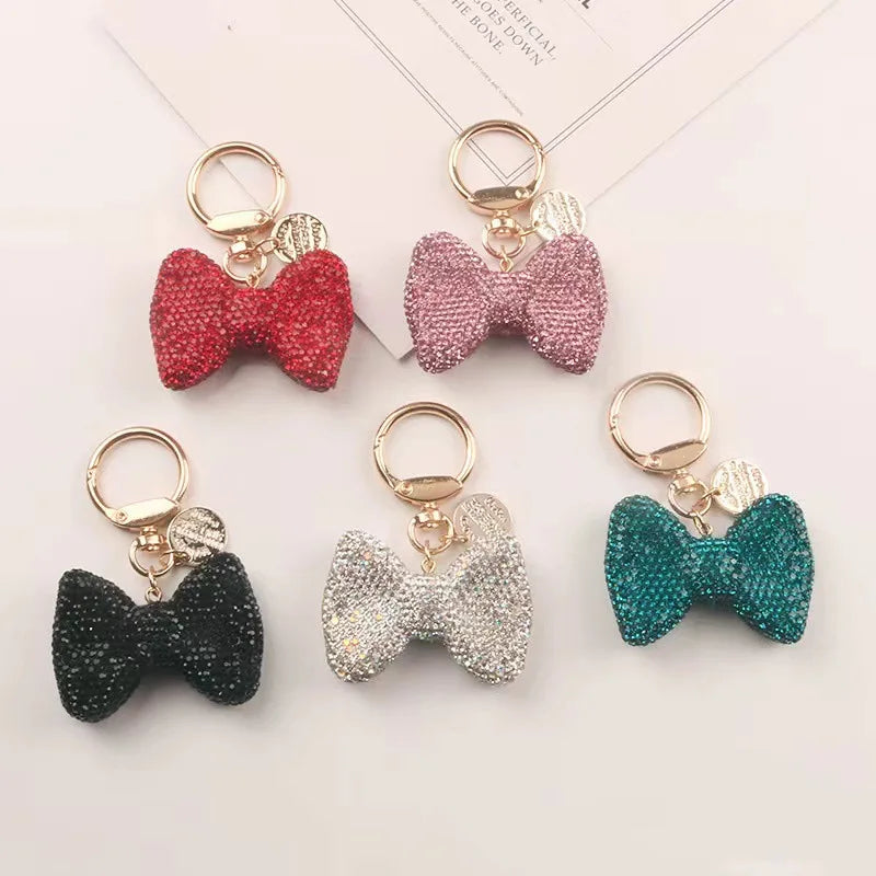 A collection of five sparkling rhinestone bow keychains in shades of pink, red, silver, and teal.