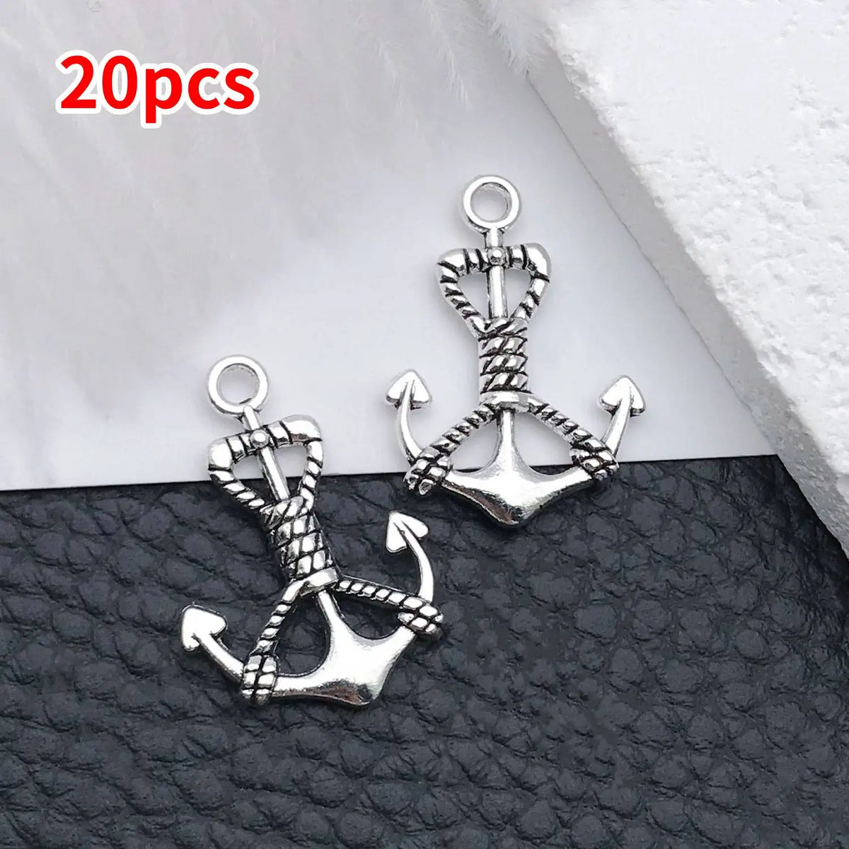 A pair of silver vintage ship anchor charms for jewelry making displayed on a black surface.