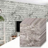A stack of 3D foam brick wallpaper panels in gray and white textures against a gray brick wall.