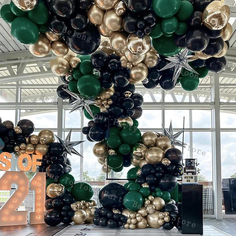A dense balloon garland featuring black, gold, and green balloons decorating an indoor space.
