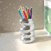 A silver disco ball spiral vase and pen holder filled with colorful pencils on a white surface.