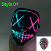 A black glow-in-the-dark LED purge mask with neon pink and blue glowing X shapes on a hand.