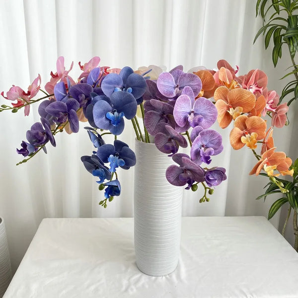A bouquet of nine artificial butterfly orchids in shades of purple, blue, and orange displayed on a white table.