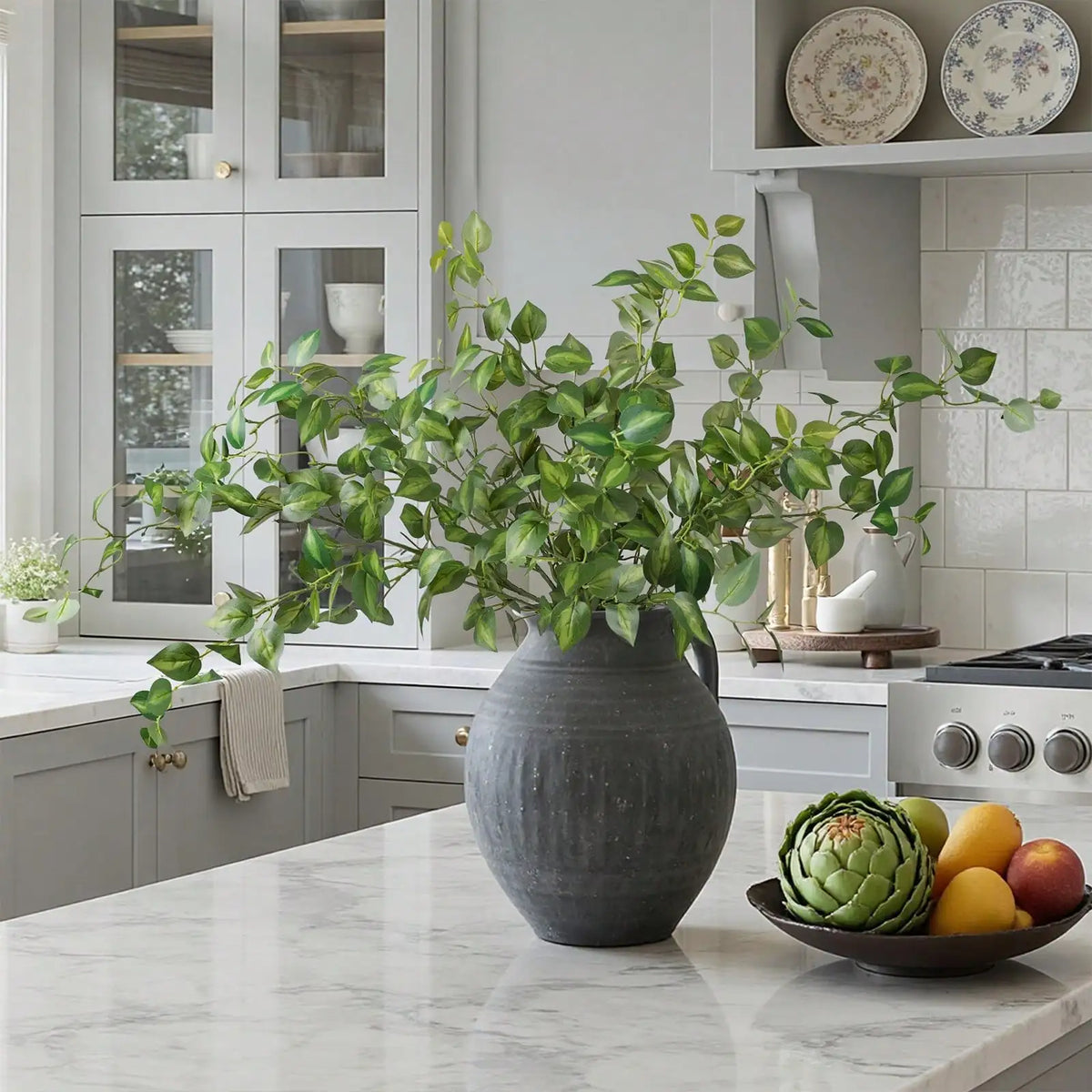 A large potted artificial eucalyptus stem with silk green leaves sits on a marble countertop.