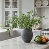 A large potted artificial eucalyptus stem with silk green leaves sits on a marble countertop.