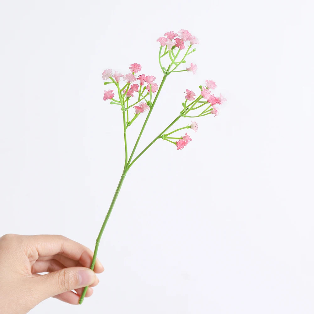 A hand holds a slender green stem with clusters of pink artificial baby's breath flowers.