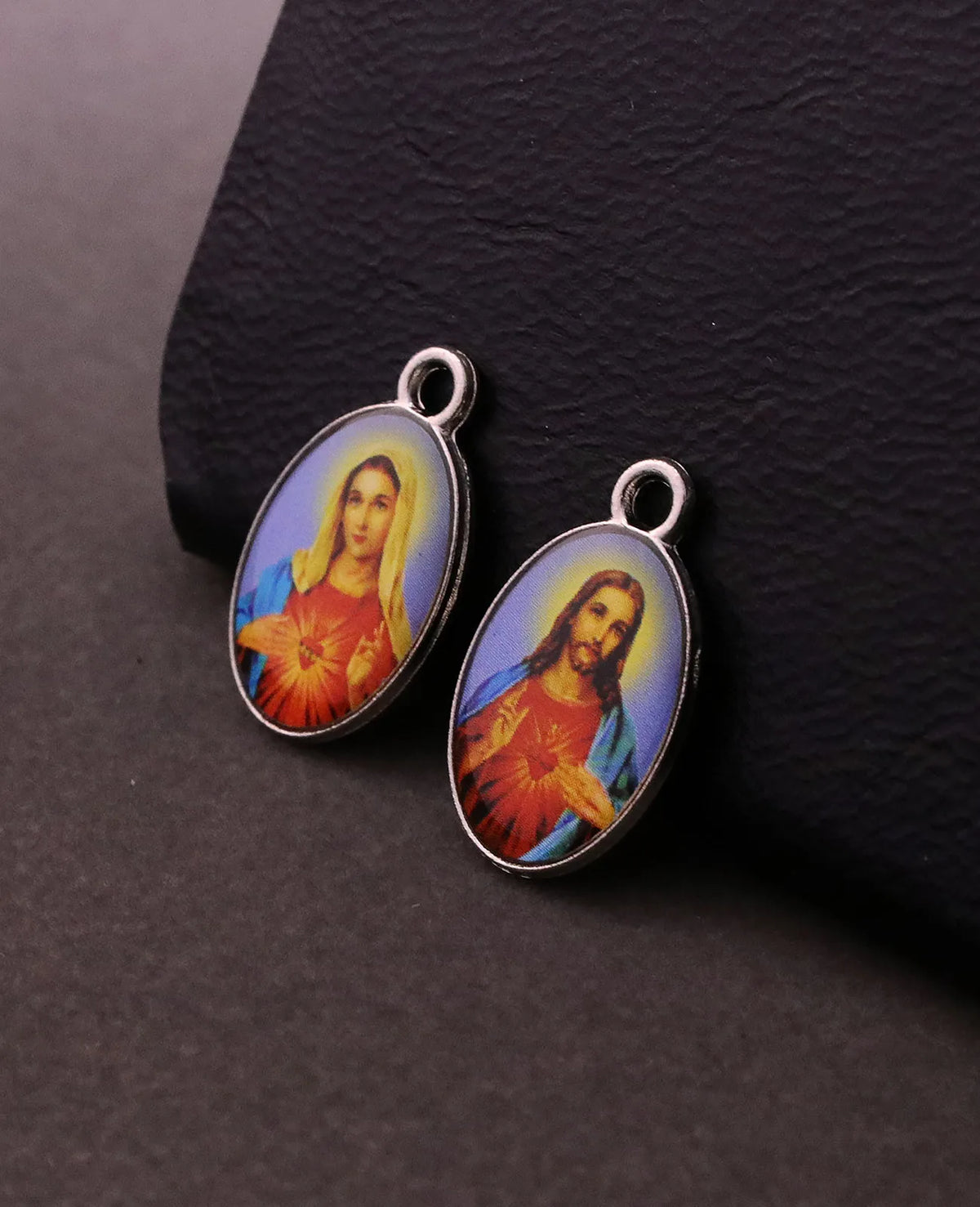 Une paire de pendentifs argentés représentant des figures religieuses, dont la Miséricorde Divine et Saint Michel, exposés su