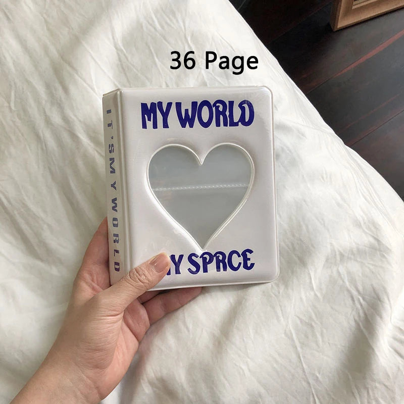 A white photo album titled My World with a heart cutout and the text My Space is held in a hand on a white bed.