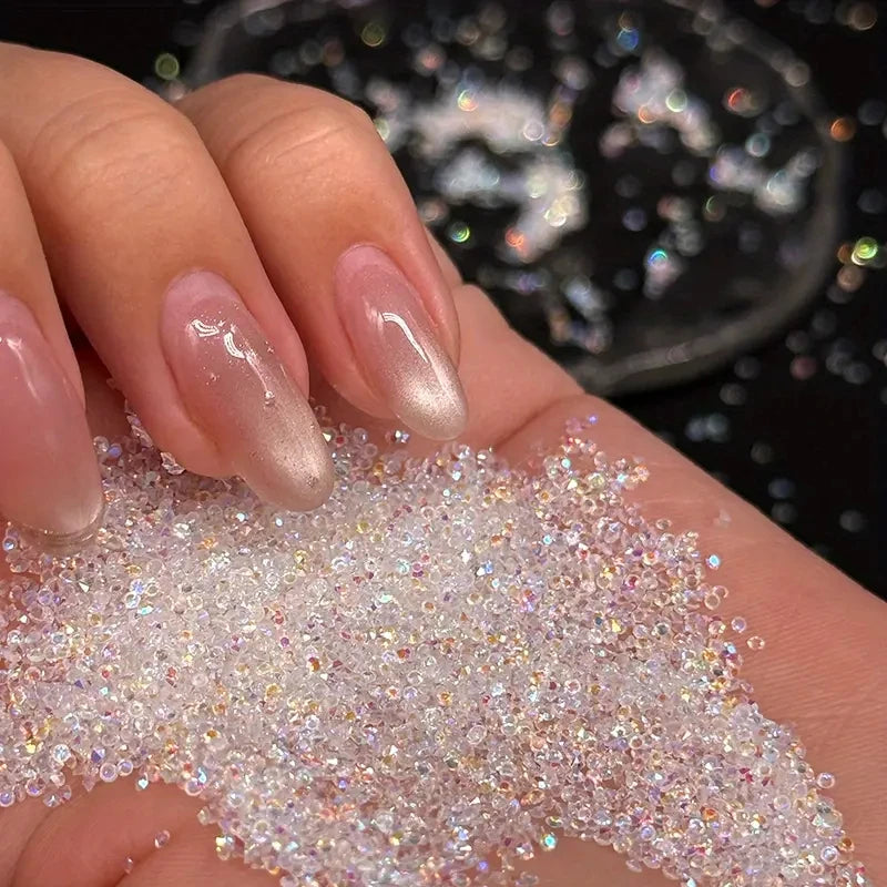 A hand holds a pile of iridescent pink nail rhinestones for DIY art against a dark background.