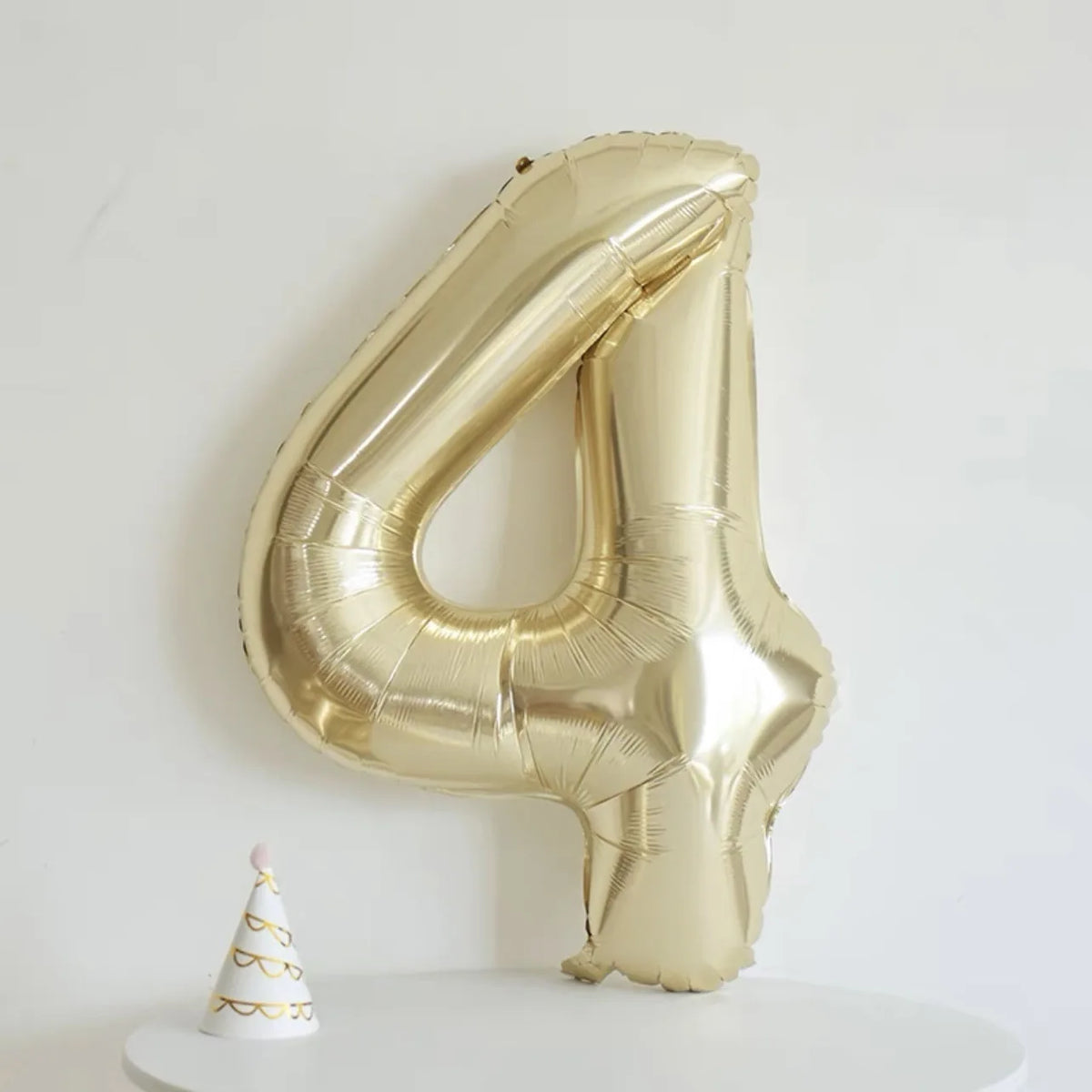A large champagne gold foil number balloon shaped like the number four displayed on a white surface.
