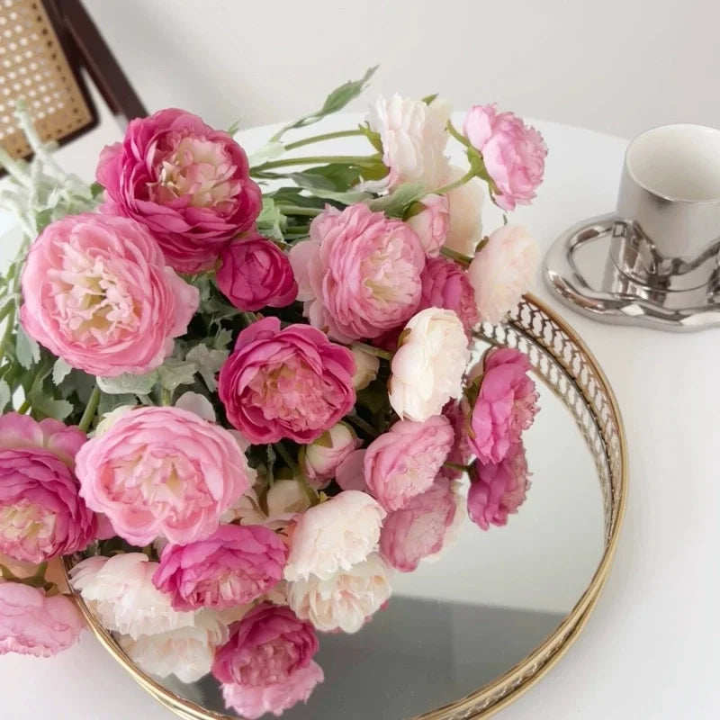 A bouquet of pink and white silk peony flowers displayed in a gold-rimmed bowl.