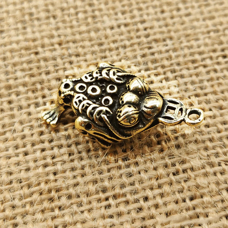 A vintage brass Chinese fortune toad charm for wealth and prosperity resting on burlap fabric.