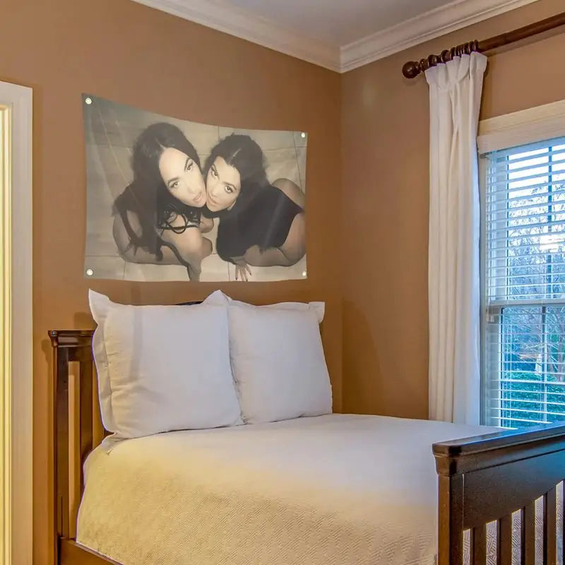 A bedroom featuring a bed with white linens and a large tapestry of two women kissing on a tan wall.
