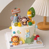 A white cake decorated with jungle safari animal toppers including a monkey, elephant, lion, and giraffe.