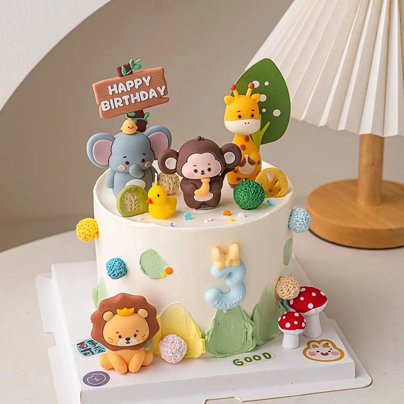 A white cake decorated with jungle safari animal toppers including a monkey, elephant, lion, and giraffe.