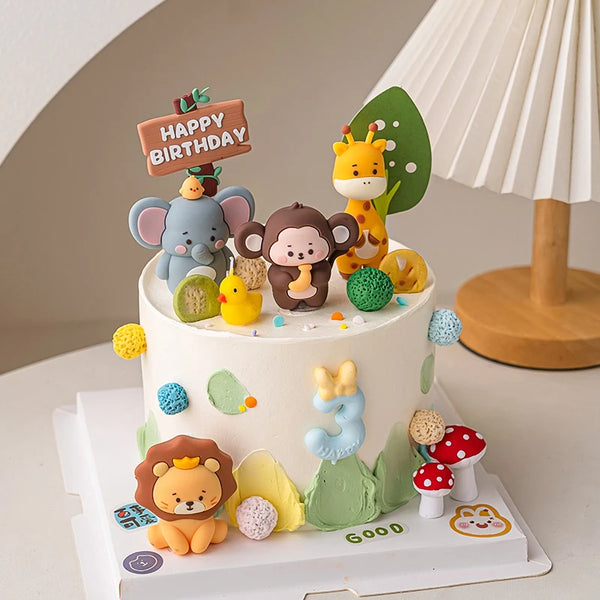 A white cake decorated with jungle safari animal toppers including a monkey, elephant, lion, and giraffe.