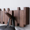 A dark wood piano key wall coat rack with eight vertical hooks mounted on a white wall.