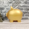 A golden pig-shaped coin storage bank sitting on a wooden surface against a textured brick background.