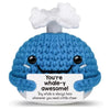 A handmade crochet blue whale potato doll with a smiling face and an inspirational card.