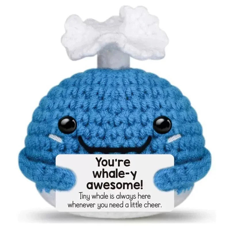 A handmade crochet blue whale potato doll with a smiling face and an inspirational card.