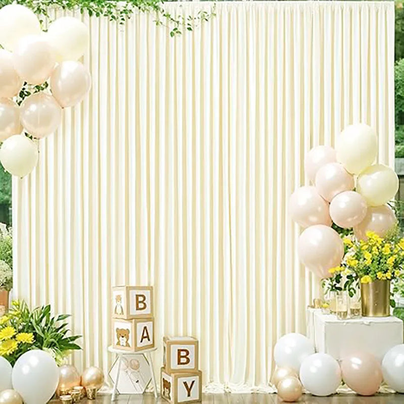 A cream-colored backdrop with vertical drapes decorated with clusters of white and blush pink balloons and floral arrangement