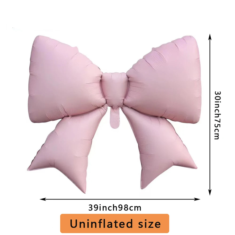 A pink bow-shaped foil balloon used for party decorations, shown flat.