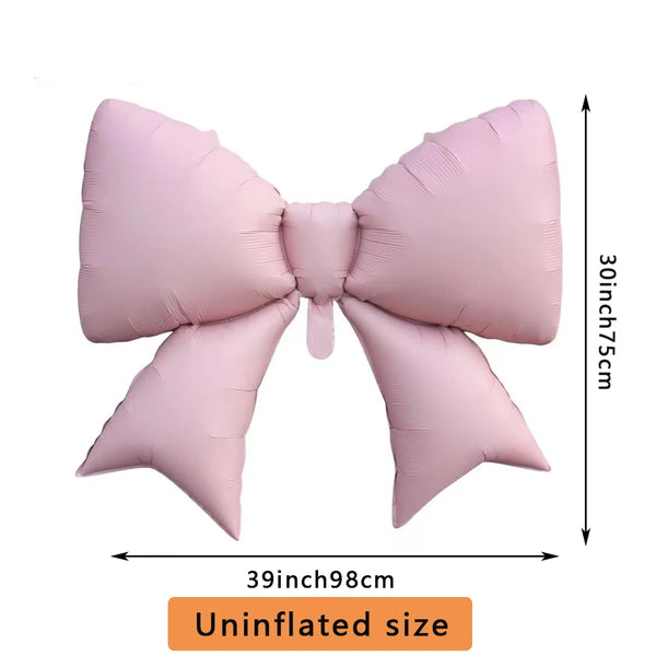 A pink bow-shaped foil balloon used for party decorations, shown flat.
