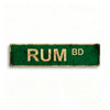 A rectangular, distressed green metal tin sign with the text RUM BD stamped in gold letters.