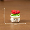 A small white ceramic pot with green leaves and red rose resin charms for craft or dollhouse decoration.