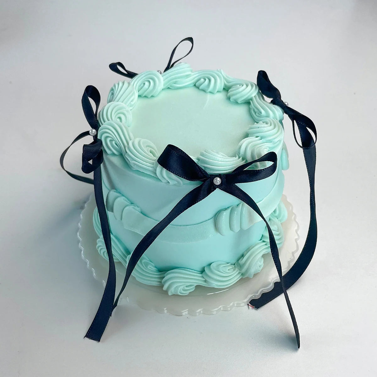 A light blue decorative fake cake with ruffled frosting and black ribbon accents.