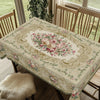 A beige floral tablecloth with pink roses and green leaves is displayed on a wooden table.