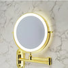 A round gold illuminated makeup mirror mounted on a marble wall.