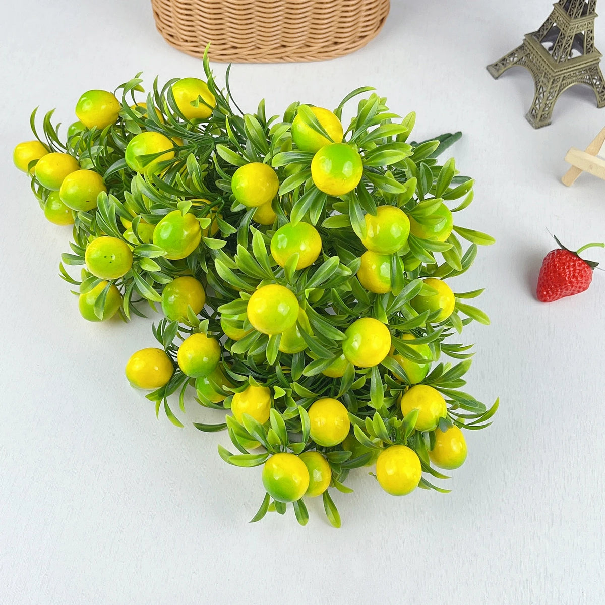 A vibrant green branch of artificial lemon leaves and small yellow fruit on a white background.