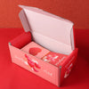 A pink luxury pop-up surprise gift box is shown open on a red surface.