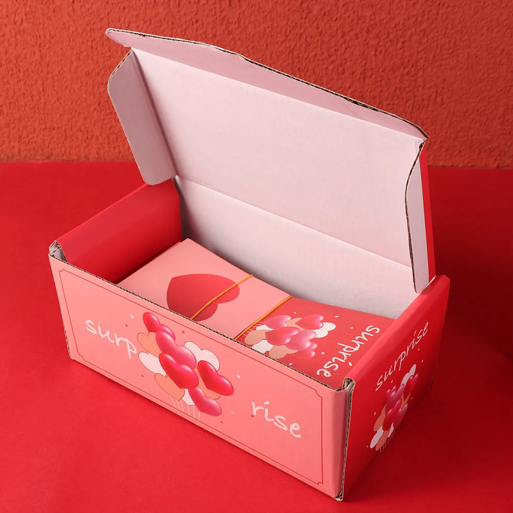 A pink luxury pop-up surprise gift box is shown open on a red surface.