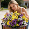 A woman holds a vibrant bouquet of artificial pansy and daisy flowers in a black planter.