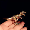 Un ornement de dinosaure en laiton solide est tenu dans la paume d'une main sur fond noir.