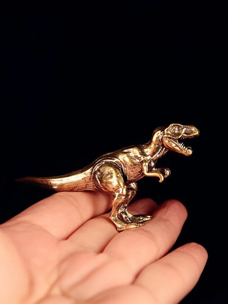 Un ornement de dinosaure en laiton solide est tenu dans la paume d'une main sur fond noir.