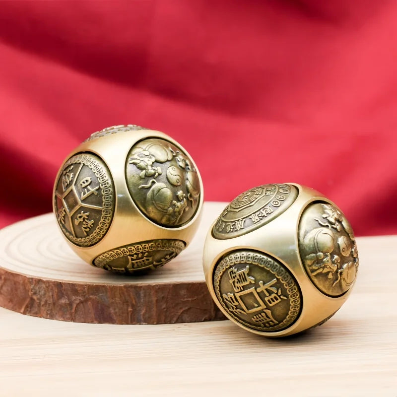 Two brass Chinese lucky coin spinners or fidget toys resting on a wooden surface with a red cloth background.