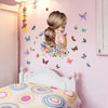 A pink wall decorated with butterfly and flower decals above a white wooden headboard.