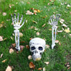 A set of realistic skeleton arm stakes and a skull for Halloween lawn decor placed in green grass with fallen leaves.