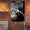 A black and white tapestry featuring a metal band logo and a figure playing a guitar hanging on a brick wall.