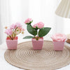 A set of three pink artificial rose potted plants displayed on a woven mat.